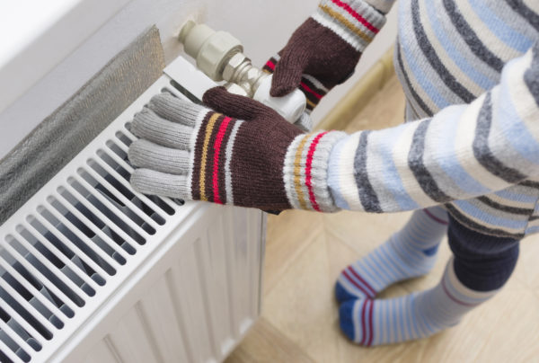 A child in woolen gloves and a sweater warms their hands near the heater.